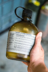 Hand holding a green canteen with a label against a blurred background