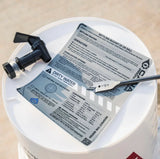 White bucket with a black valve and label on concrete surface
