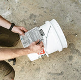 Person placing a label on a white bucket on a concrete floor