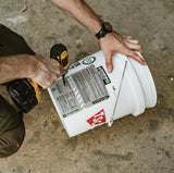 Person drilling a hole in a white bucket on a concrete floor