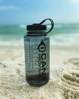 smoke grey nalgene water bottle with black lid and cana provisions logo on a sand beach background