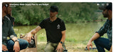 A man from cana provisions in a black t-shirt with a white cana provisions logo sits outdoors by a river, holding a product package, with two other men from dirty civilian youtube channel seated on either side in a natural outdoor setting.