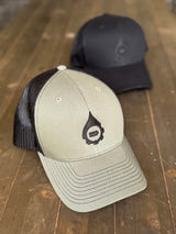 Two baseball caps on a wooden surface, one beige with black mesh and logo, the other black.