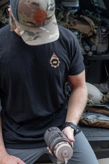 A man in a black t-shirt and camouflage cap holds a tan water bottle while sitting on the tailgate of a truck