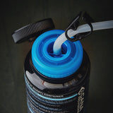 Close-up of a black water bottle with a bright blue cap, showing a clear tube inserted into the opening and the black cap resting beside it on a dark surface.