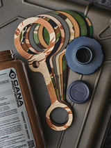 Set of camouflage-patterned water bottle cap tethers next to a black bottle cap on a green case