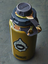 olive green water bottle with camouflage-patterned cap and strap on a gray surface