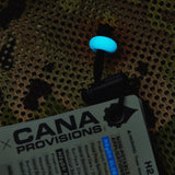 A glowing blue illuminated bead, resting on a camo mesh bag next to a CANA Provisions tag.