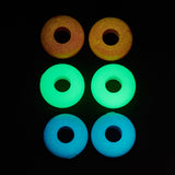 Three pairs of glow-in-the-dark donut-shaped beads arranged in a grid on a black background, showing yellow, bright green, and bright blue colors.