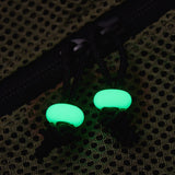 Two glowing green donut-shaped beads on black zipper pulls, placed on a dark olive green mesh fabric background.