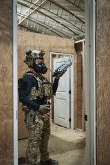 Person in tactical gear holding a cana provisions water bottle in a wooden house