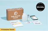 Tap Score at home water test kit displayed on a light blue background, including a brown cardboard box, reagent bottle, test strip vial, smartphone, and printed result cards. A circular 'Our Pick Wirecutter 2025' badge appears in the top right, and a yellow banner at the bottom reads '111 Analytes Tested'.