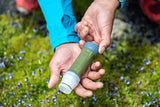 Person holding a green water filter with a blue cap in a natural setting