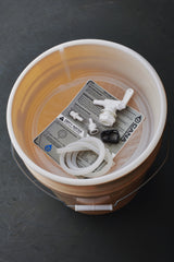 Bucket with plumbing parts and a label on a dark surface