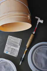 water filter components on a tan bucket with labels and hoses on a dark background