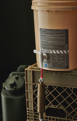 water filter components on a tan bucket with labels and hoses on a dark background