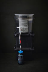 water filter components on a grey bucket with labels and hoses on a dark background